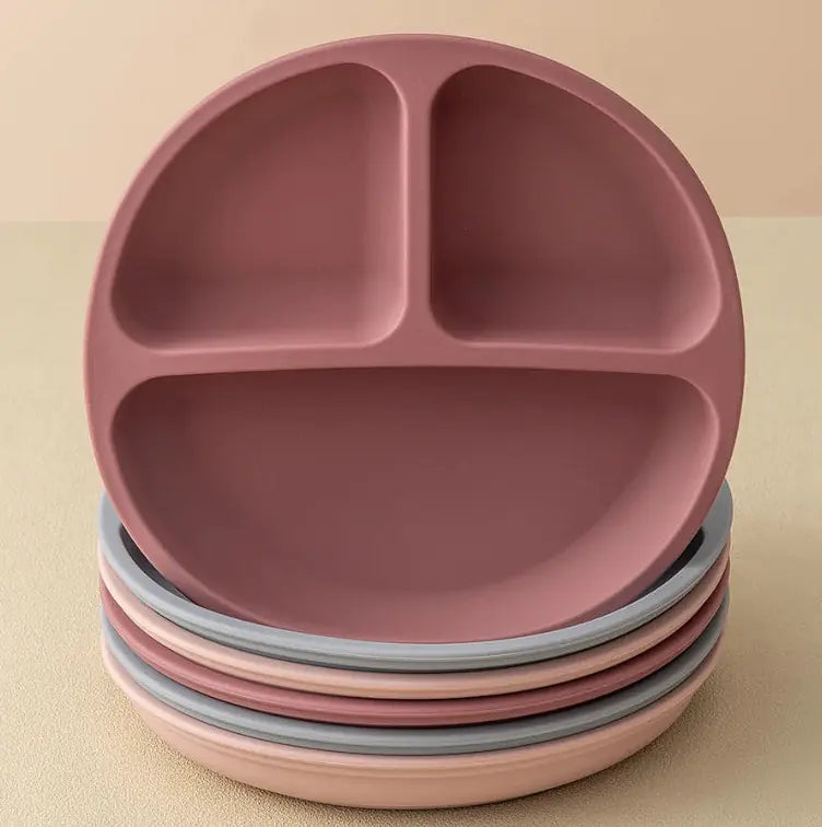 A stack of matte divided baby plates in a dusty rose pink color, with one larger plate on top and smaller plates underneath, set against a warm beige background.